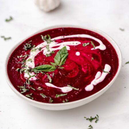 Soupe rouge vif aux betteraves dans un bol avec filet blancs de yogourt nature et parsemée de feuilles de basilic frais