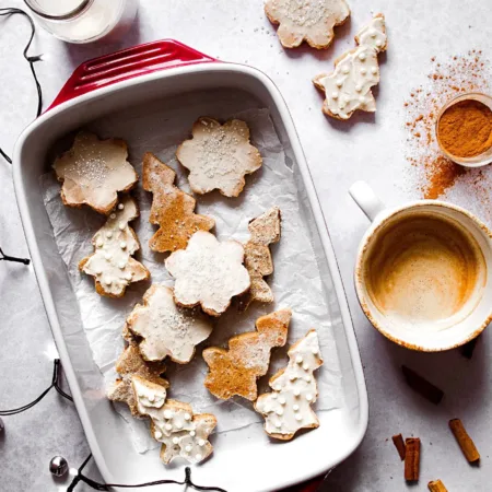 Plat rempli de biscuits en formes de flocons et de sapins décorés pour Noël avec une tasse de café