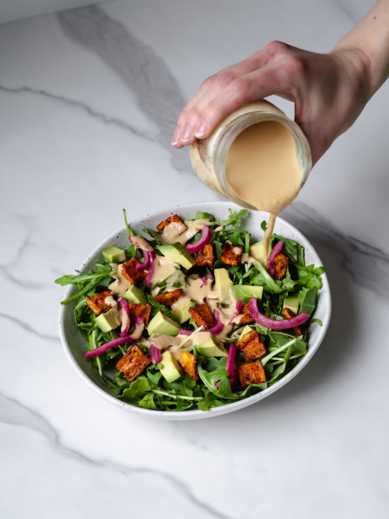 Grand bol de salade de patates douces rôties et avocat avec une vinaigrette aux arachides qui est versée sur le dessus