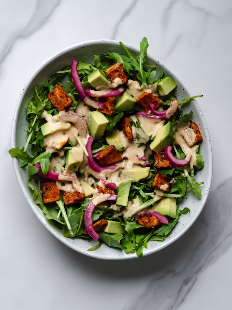 Grand bol de salade de patates douces rôties et avocat avec une vinaigrette aux arachides sur le dessus