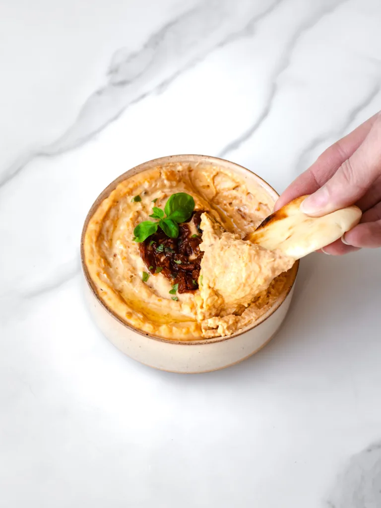 Main qui trempe dans un hummus maison de haricots blancs aux tomates séchées