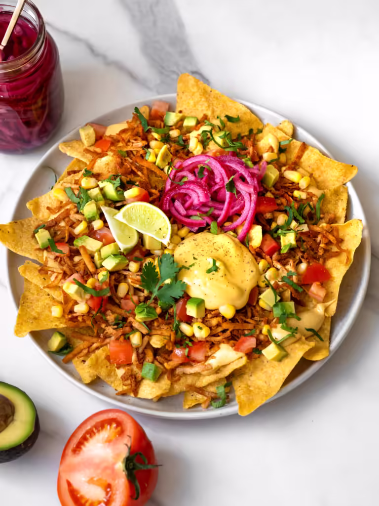 Assiette débordante de nachos tout garnis végétaliens avec tofu effiloché et sauce au fromage