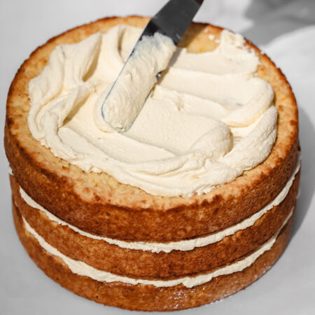 Glaçage santé et versatile à base de tofu (sans huile ni beurre) en train de se faire étendre à la spatule sur un gâteau de fête au citron