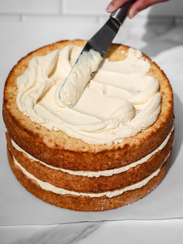 Glaçage santé et versatile à base de tofu (sans huile ni beurre) en train de se faire étendre à la spatule sur un gâteau de fête au citron