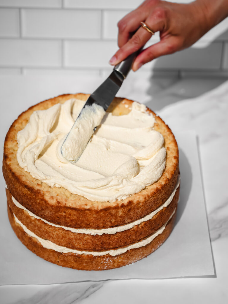 Glaçage santé et versatile à base de tofu (sans huile ni beurre) en train de se faire étendre à la spatule sur un gâteau de fête au citron